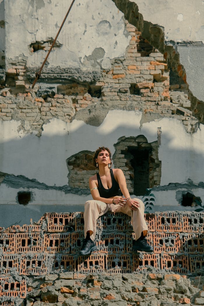 A woman sitting against a backdrop of rugged, decaying urban ruins, exuding resilience.
